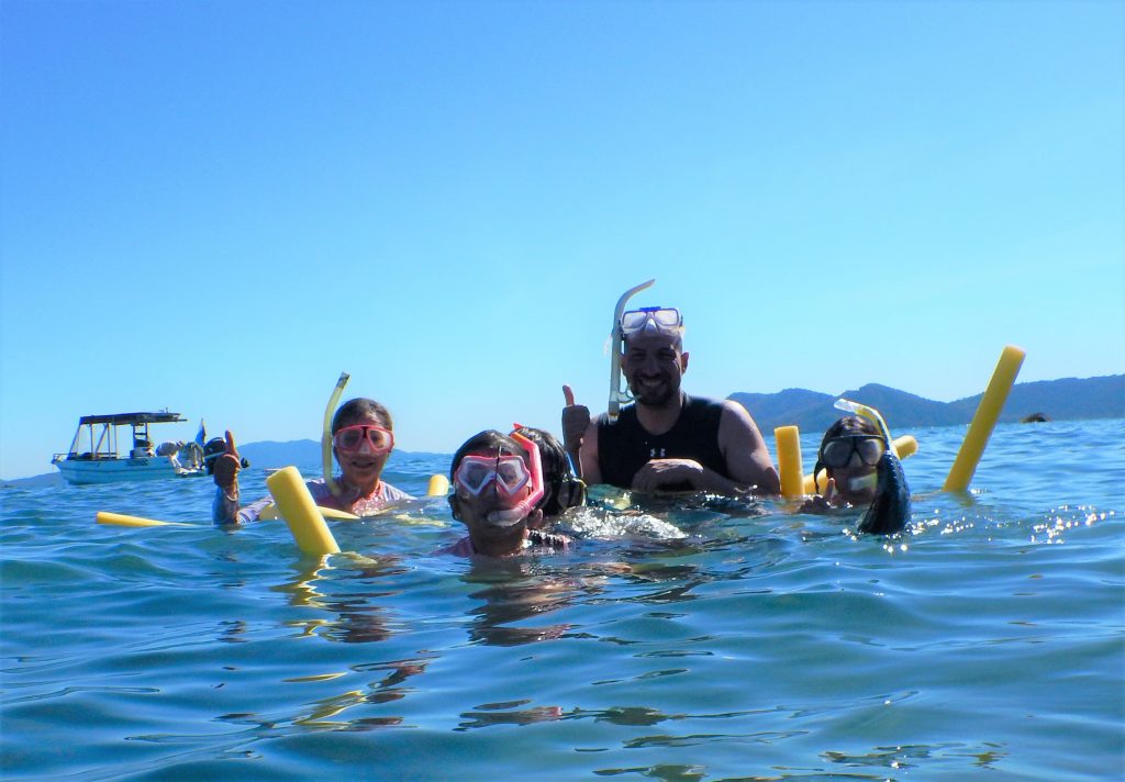 A family floats in a tropical sea with snorkelling gear giving the thumbs up